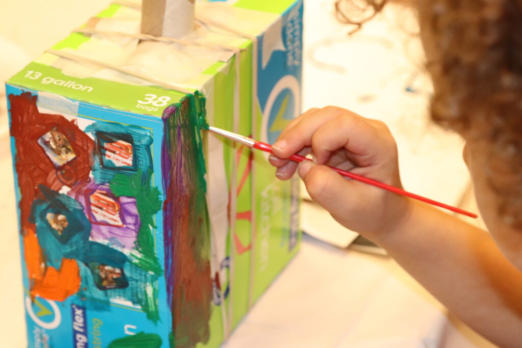 A young boy paints a tissue box.