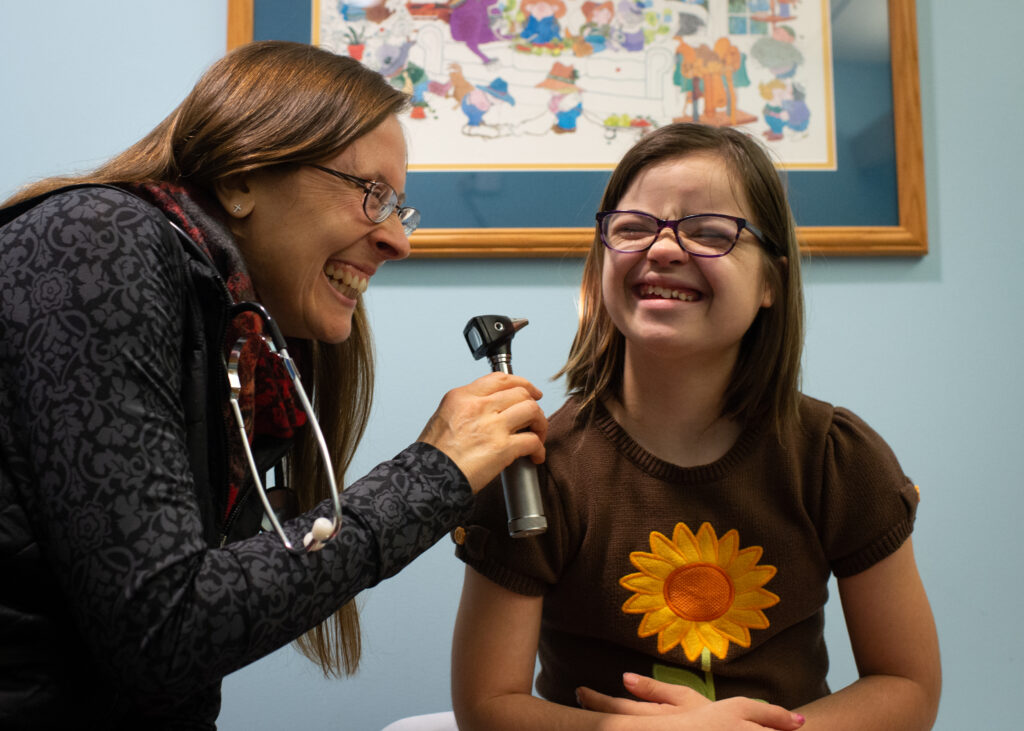 young girl and woman doctor smiling while the woman doctor holds up an Otoscope
