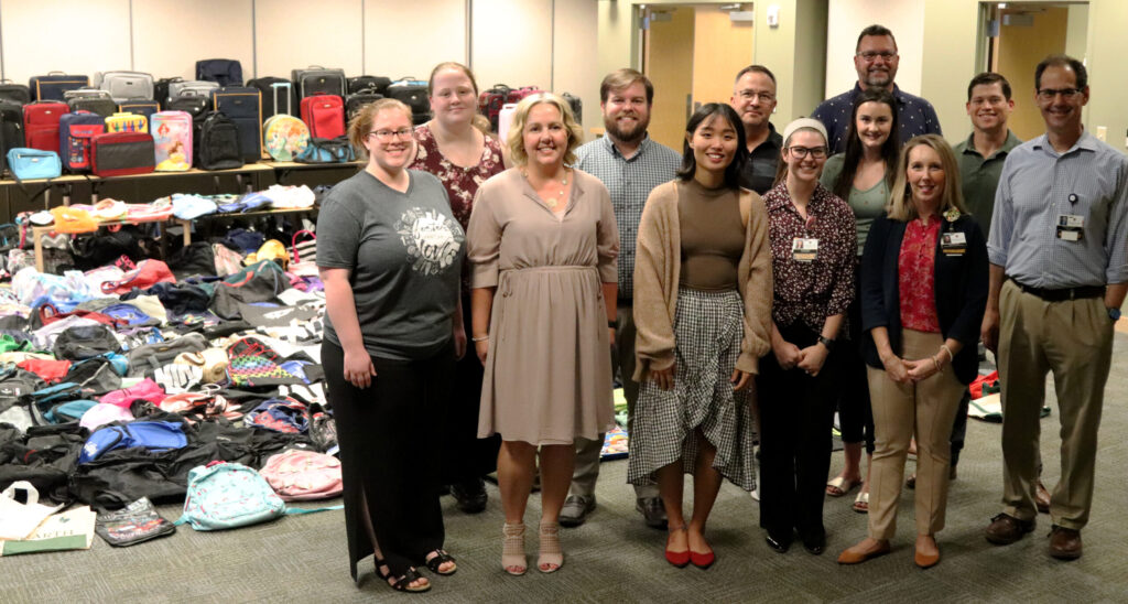 Representatives from the Thompson Center, Veterans United Home Loans, and the Central Missouri Foster Care and Adoption Agency pose in front of hundreds of backpacks and suitcases.